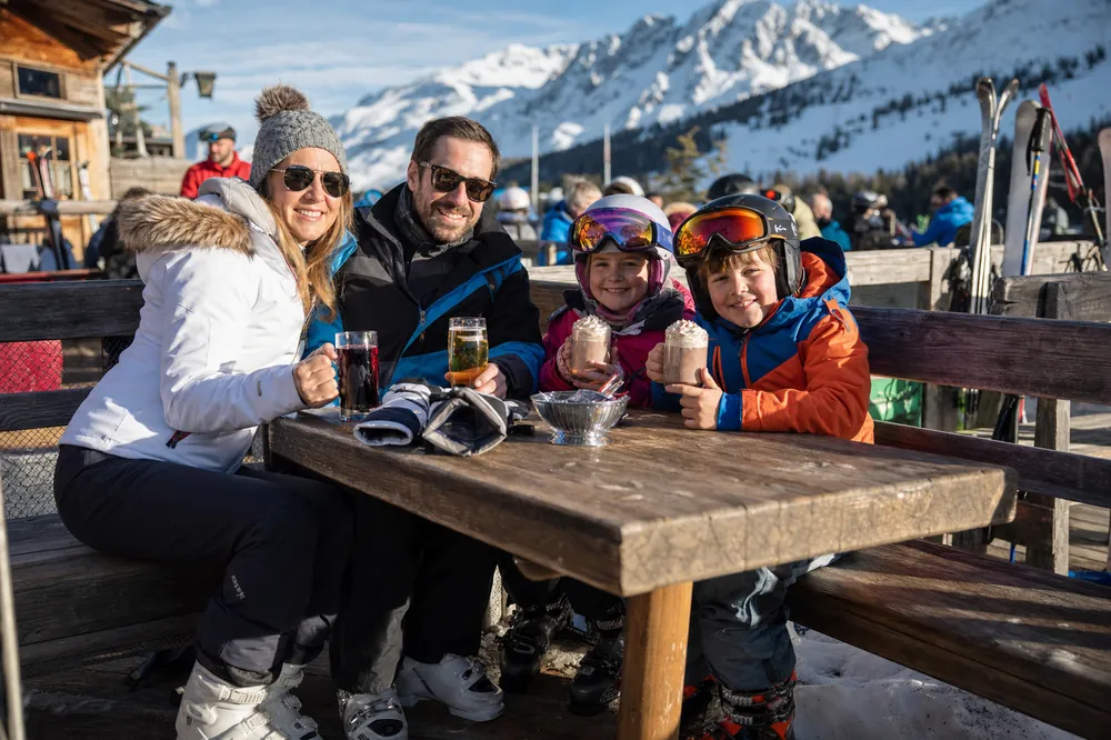 Family with hot chocolate on a sunny terrace by the piste